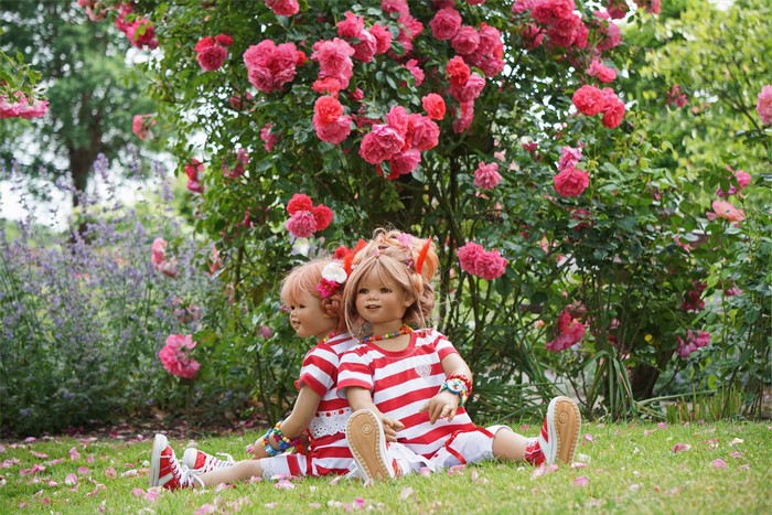 Two dolls sitting in a rose garden