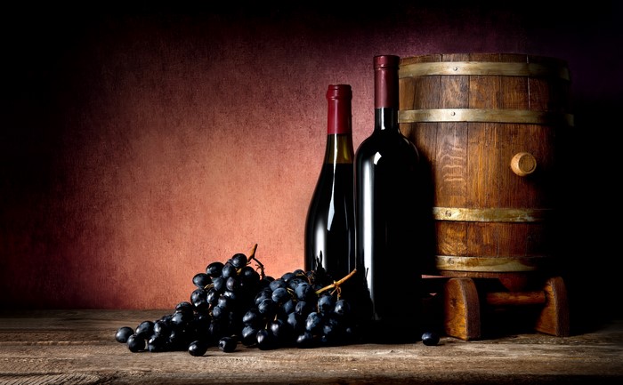 Wine bottles, grapes, and barrel on a wooden table