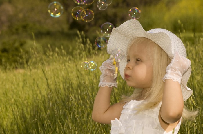 Little girl in hat blowing soap bubbles