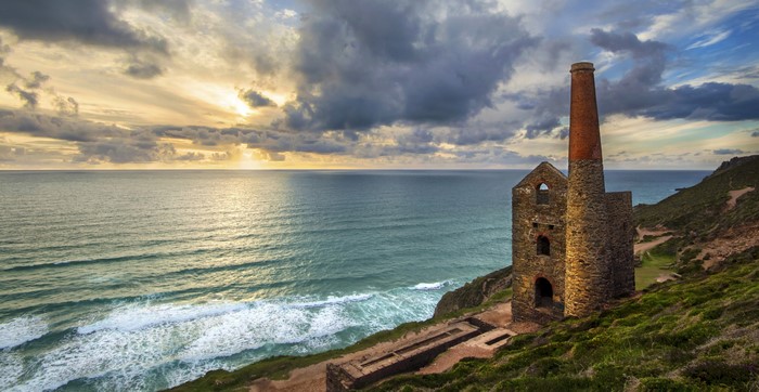 Ruined mine building and chimney by the sea at sunset