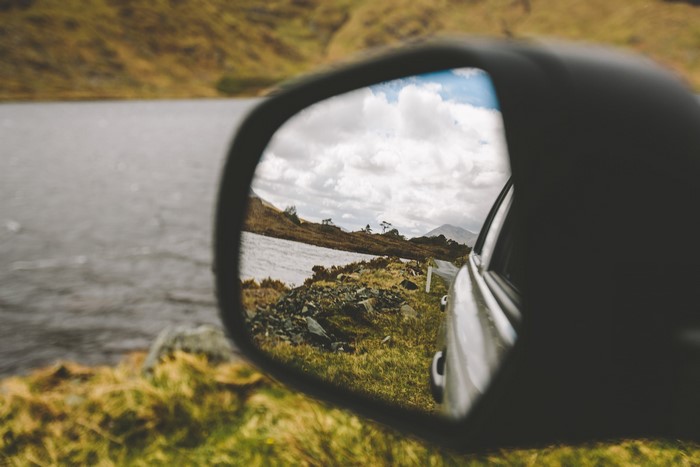 Car side mirror reflecting a lake and hills