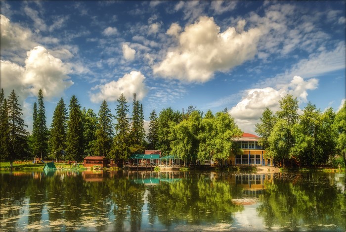 Building by the river with trees and clouds