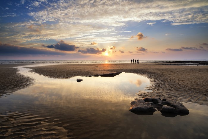 People walking on beach at sunset with reflection in puddle