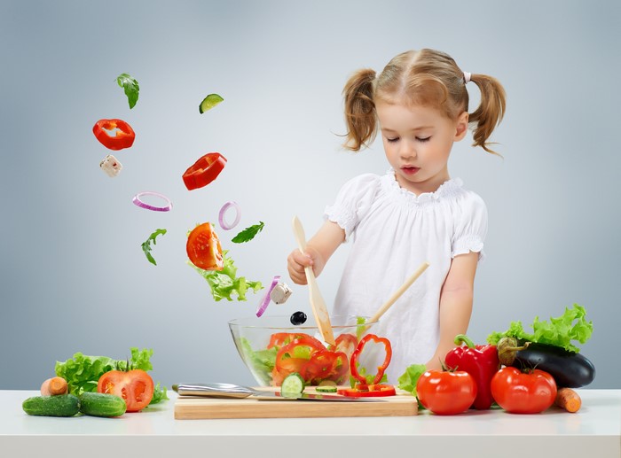 Little girl making a salad with flying vegetables