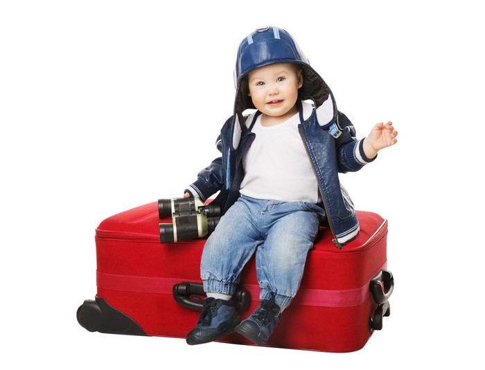 Baby in winter hat and jacket on suitcase with binoculars