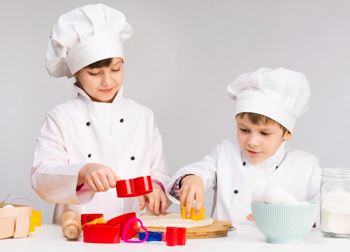 Two children in chef uniforms baking