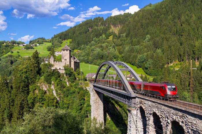 Red train crossing a stone bridge in Austria