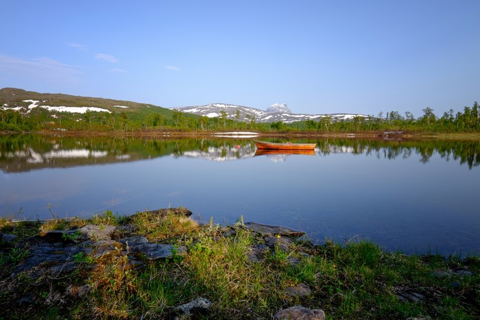 Orange boat on a calm lake with snowy mountains in the background