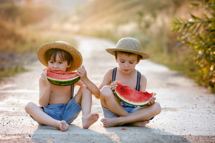 Two boys in hats eating watermelon