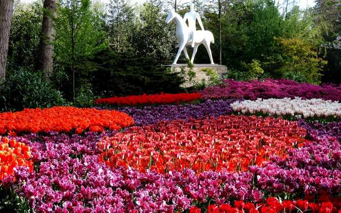 Sculpture of a person on a horse in a garden with tulips