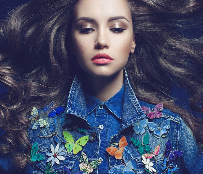 Woman with long brown hair wearing a denim jacket adorned with butterflies