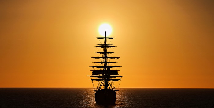 Silhouette of a sailing ship against the sun