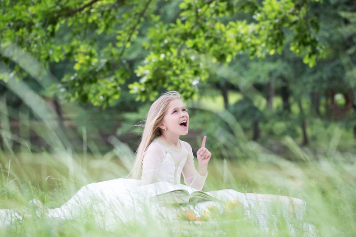 Little girl in a white dress reading a book in grass