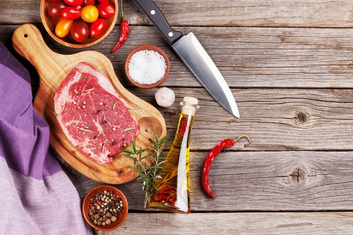 Raw steak with spices and knife on wood