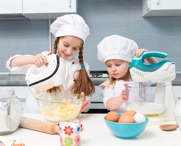 Two young girls in chef uniforms baking in a kitchen