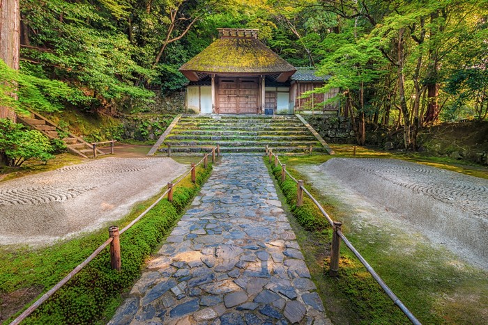Stone path leading to a traditional Japanese temple with a thatched roof