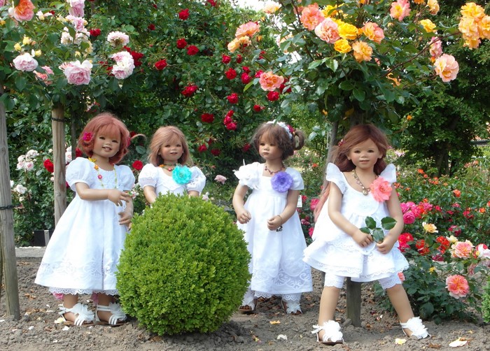 Four dolls dressed as little girls in a rose garden