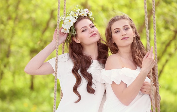 Two beautiful women with flower wreaths on a swing
