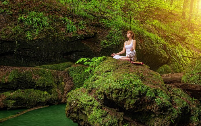 Woman meditating on mossy rocks in a forest
