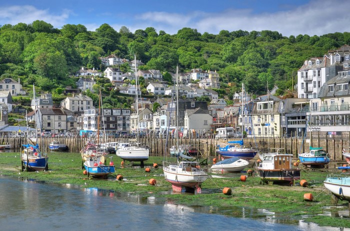Boats moored in a harbor with houses on a hill in Looe, England