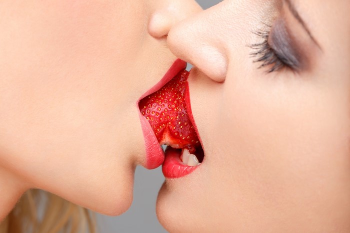 Two faces kissing over a strawberry