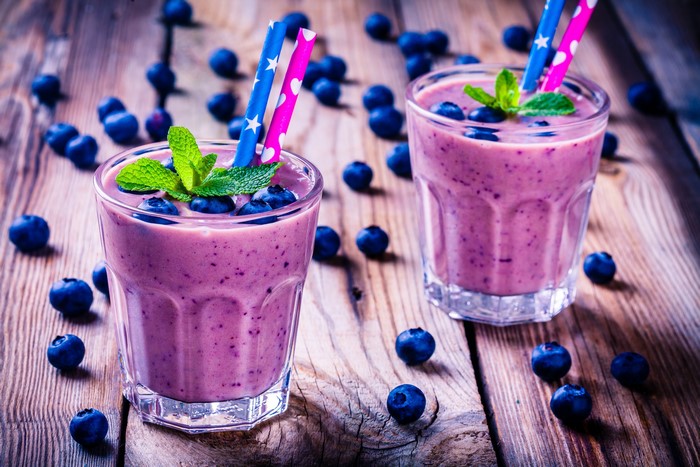 Two blueberry smoothies with mint and blueberries on wood planks