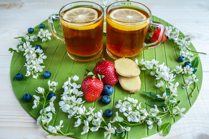 Two cups of tea with lemon, strawberries, blueberries, and ginger