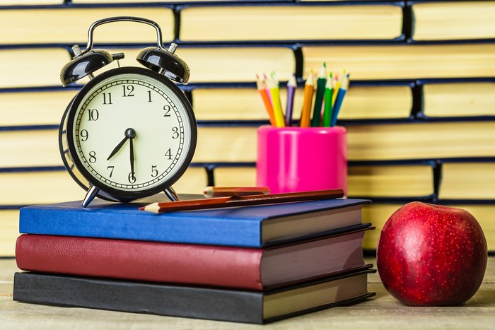 Alarm clock on books with apple and pencils
