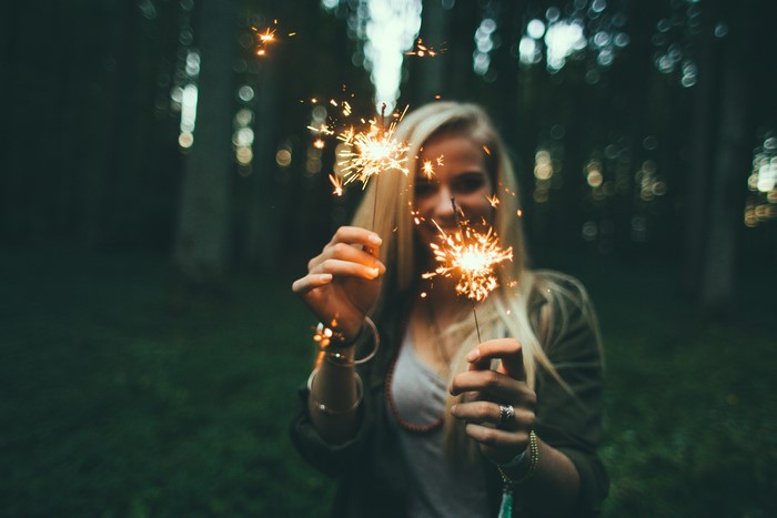 Blonde girl holding sparklers in a forest