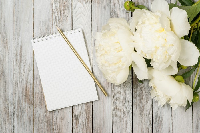 White peonies and a notepad with a pencil on wood planks