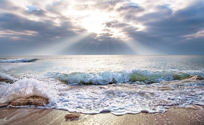Sea waves and sun rays over the horizon