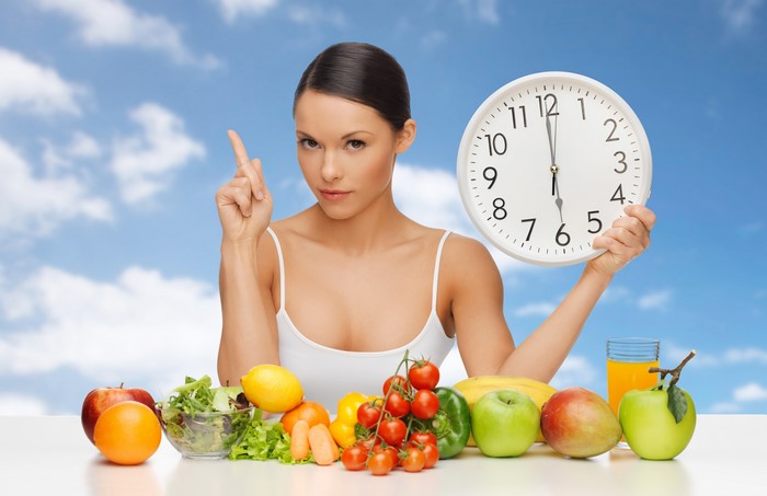 Woman holding clock with fruits and vegetables