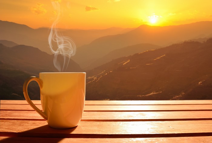 Mug of steaming coffee with mountain sunrise