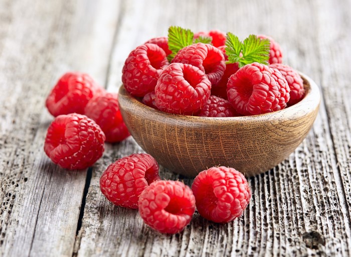 Raspberries in a wooden bowl on wood planks
