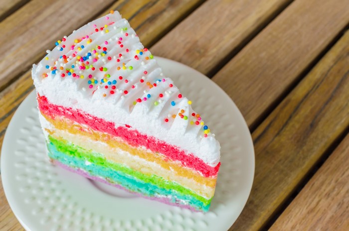 Slice of rainbow cake with sprinkles on a saucer