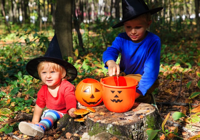 Two children in Halloween costumes with pumpkin buckets