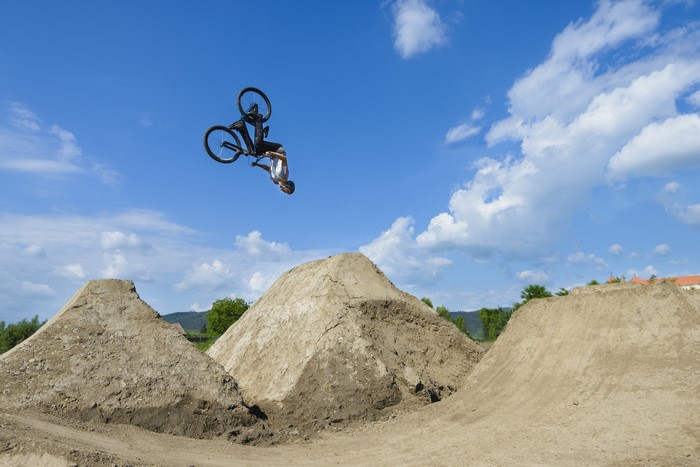 Man doing a flip on a bicycle over dirt jumps