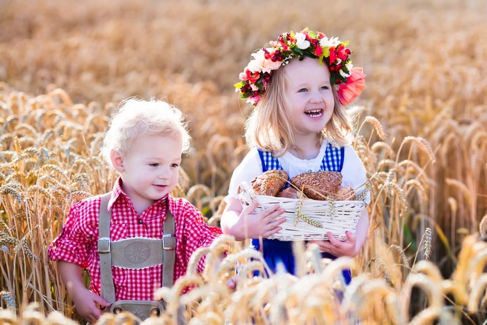 Two children in a wheat field with a basket of buns