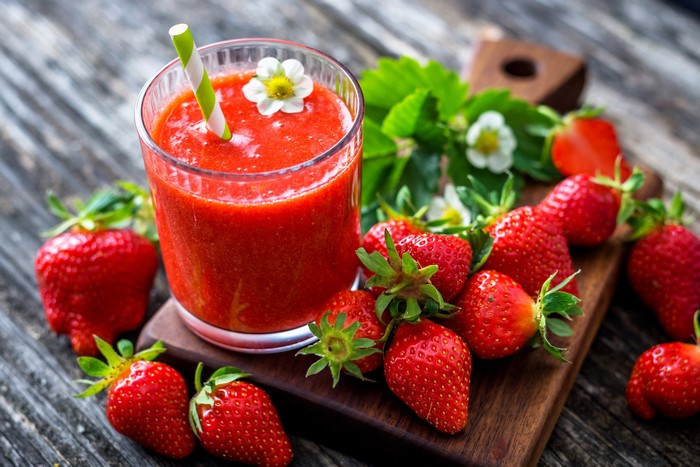 Strawberry juice in a glass with strawberries on a cutting board