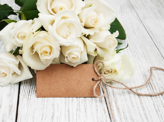 White roses with a blank tag on a wooden surface