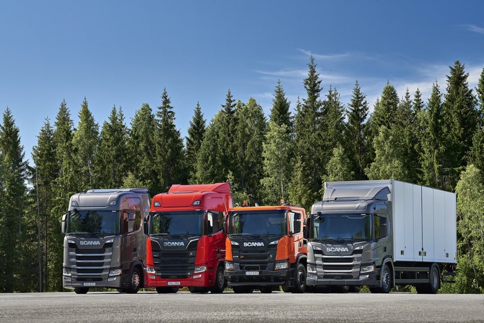 Four Scania trucks parked in front of a forest