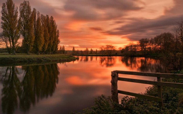 River reflecting sunset sky with trees and fence