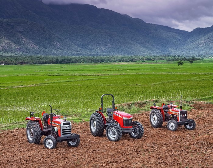 Three Massey Ferguson tractors in a field with mountains