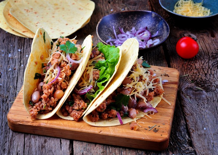 Tacos with ground meat, beans, cheese, and lettuce on a cutting board