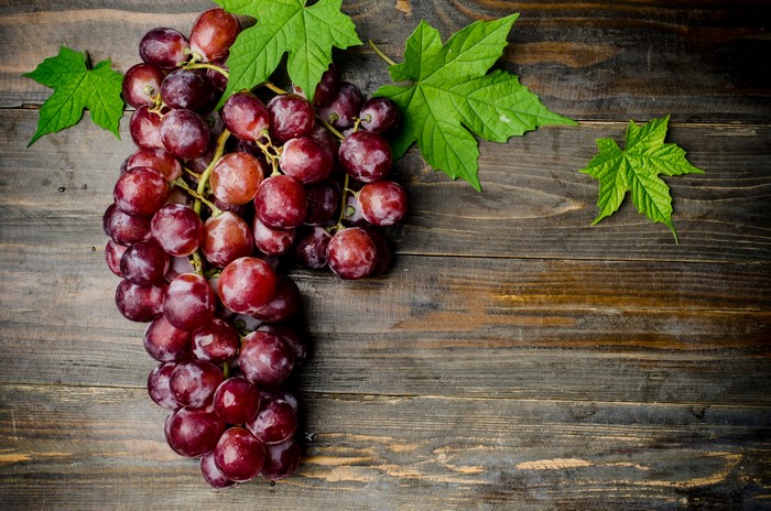 Red grapes with green leaves on wood planks