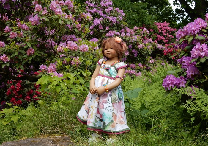 Doll in a floral dress in a garden with rhododendrons