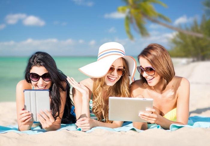 Three women with tablets on a beach
