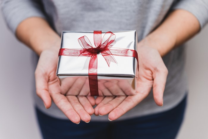Hands holding a silver gift box with a red ribbon