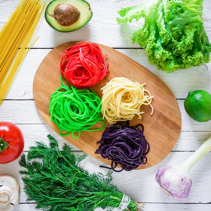 Multicolor spaghetti on a cutting board with fresh ingredients