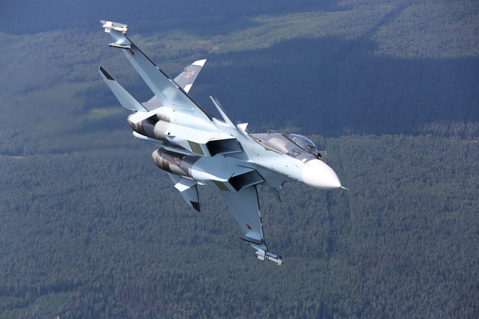 Sukhoi Su-30SM fighter jet flying over a forest